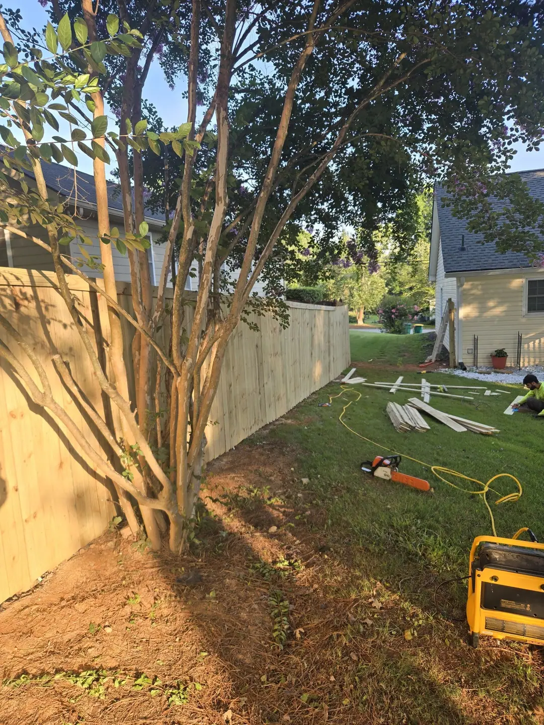 A CnC Fences crew member cutting boards on the lawn beside a new wood privacy fence
