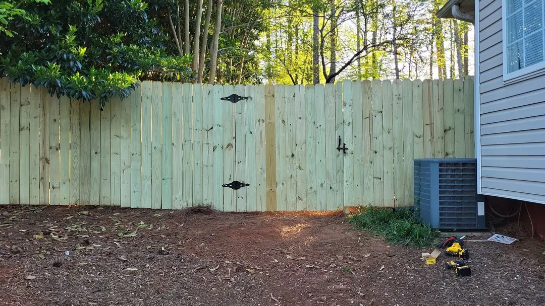 New wood privacy fence with a double gate and black strap hinges beside a house