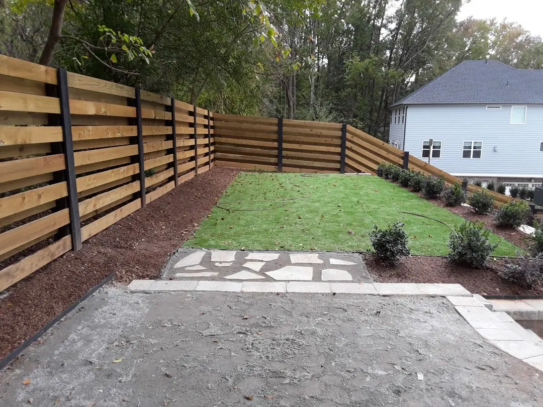 Horizontal board fence with black posts around a new lawn and stone path