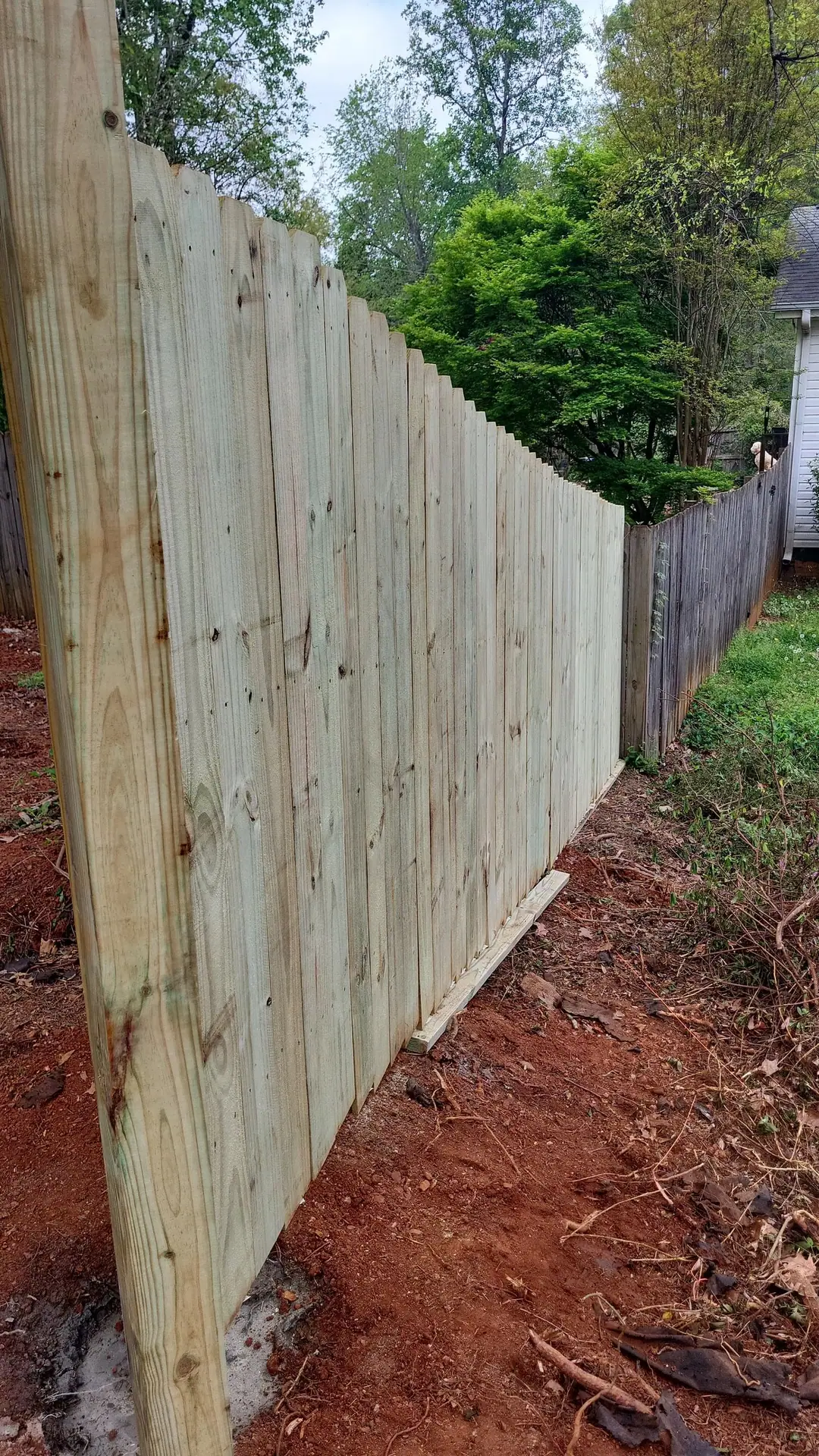 Dog-ear wood fence run with fresh boards along red Georgia clay